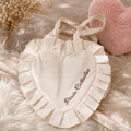 Cream heart-shaped tote bag with pleated ruffle trim and embroidered Pixie Collective logo, styled with dried flowers and a pink heart pillow